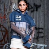 Person wearing a blue hoodie with text, sheer top, and white skirt against a graffiti-covered wall.