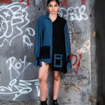 Person wearing a blue shirt over a black dress against a graffiti-covered wall.