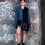 Person wearing a blue shirt over a black dress against a graffiti-covered wall.