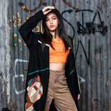Person wearing an orange top and patterned coat in front of a graffiti-covered wall