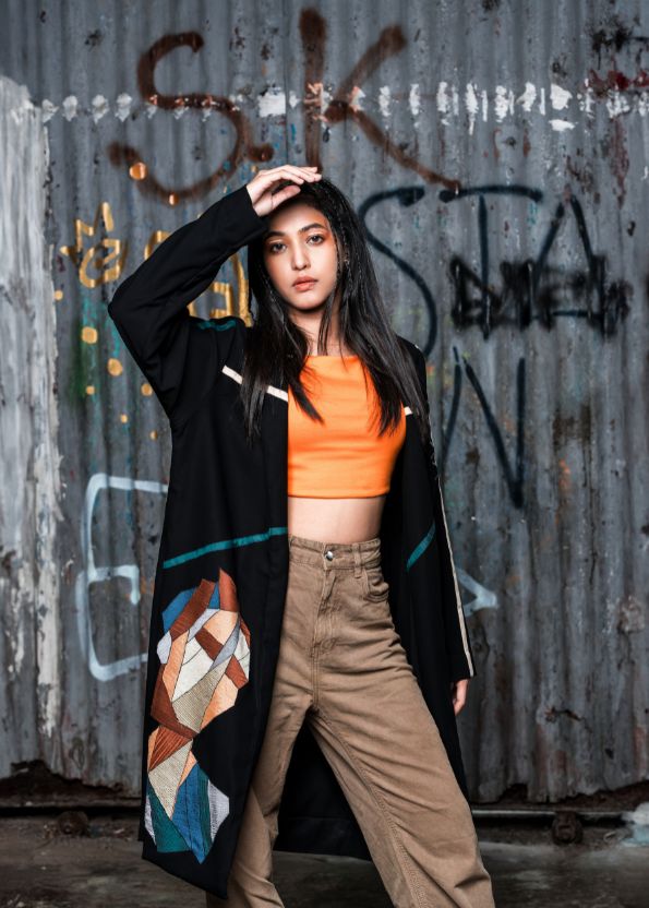 Person wearing an orange top and patterned coat in front of a graffiti-covered wall