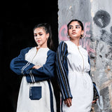 Two women in matching outfits standing against a textured wall.