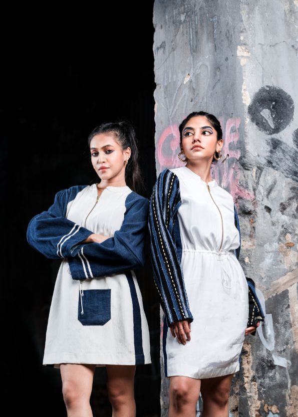 Two women in matching outfits standing against a textured wall.