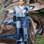 Person wearing a blue and gray outfit standing in front of a colorful, abstract background.