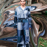 Person wearing a blue and gray outfit standing in front of a colorful, abstract background.