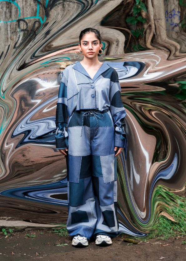 Person wearing a blue and gray outfit standing in front of a colorful, abstract background.
