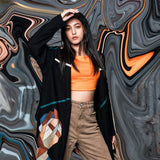 Person wearing an orange top and brown pants against a swirling abstract background