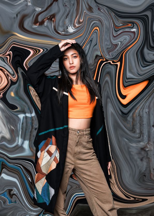 Person wearing an orange top and brown pants against a swirling abstract background