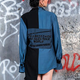 Person wearing a blue and black jacket with text, standing against a graffiti-covered wall.