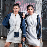 Two women wearing matching white dresses with blue accents against a graffiti-covered wall.