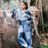 Person wearing a blue patchwork outfit standing in front of a graffiti-covered wall.