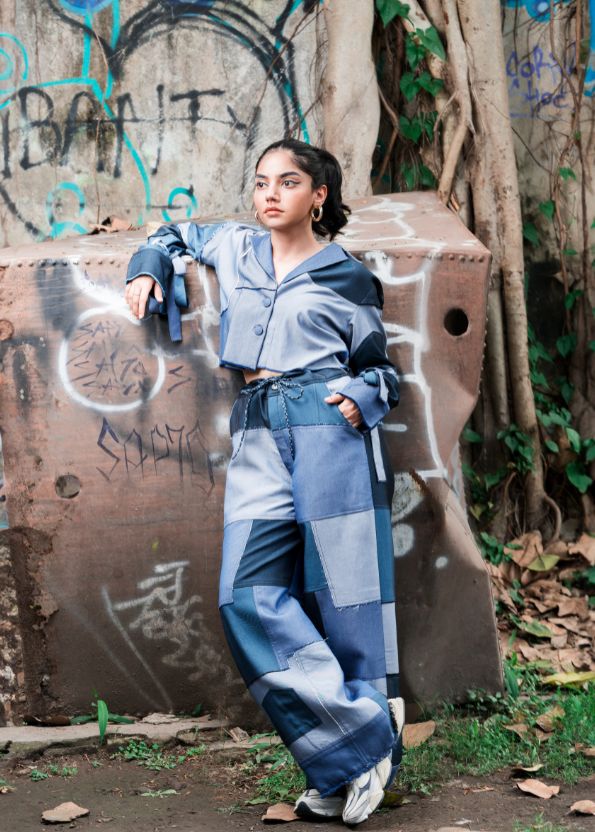 Person wearing a blue patchwork outfit standing in front of a graffiti-covered wall.
