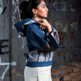 Woman wearing a blue jacket over a white top in front of a graffiti-covered wall.