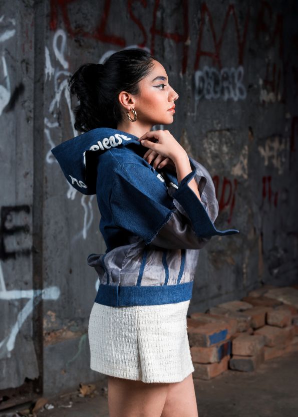 Woman wearing a blue jacket over a white top in front of a graffiti-covered wall.