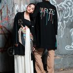 Two people standing against a graffiti-covered wall.