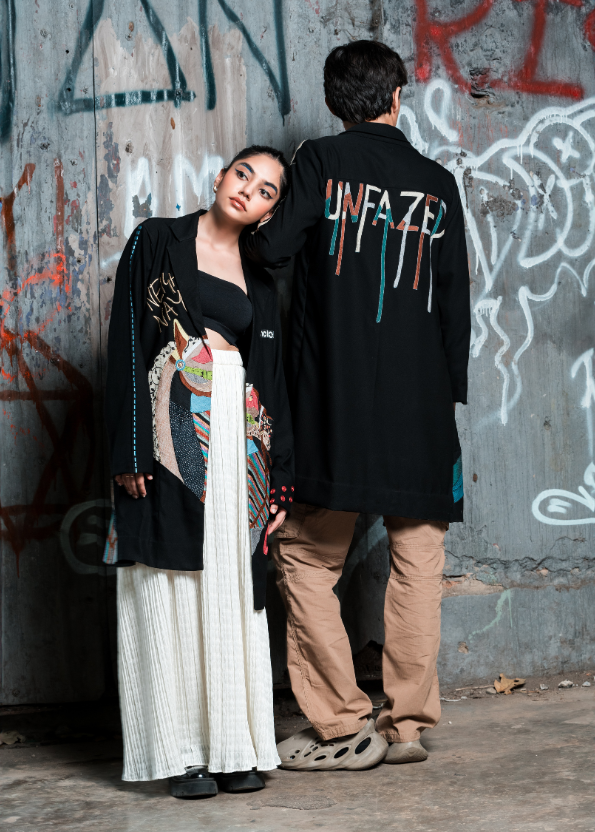 Two people standing against a graffiti-covered wall.