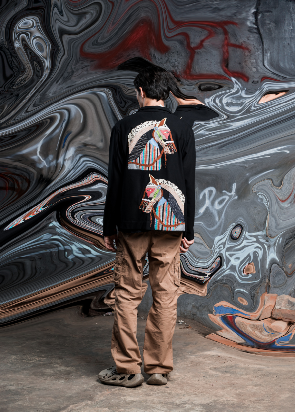 Person wearing a black hoodie with colorful designs standing in front of a large abstract mural.