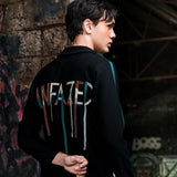Person wearing a black hoodie with colorful text on the back against a graffiti-covered wall.