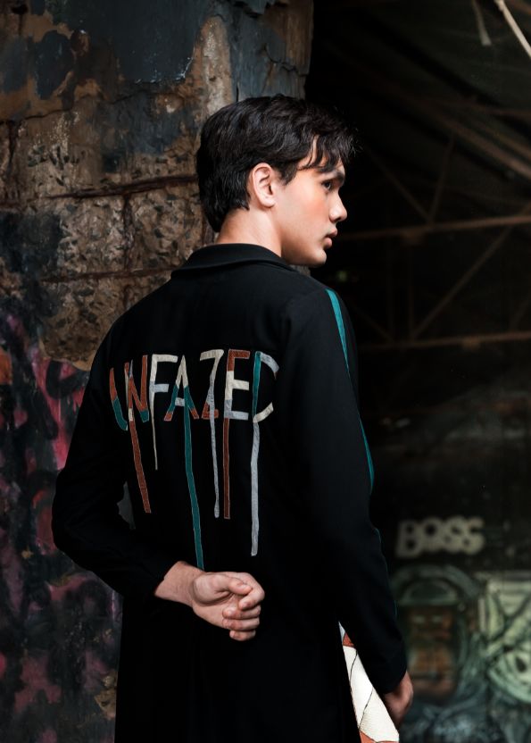 Person wearing a black hoodie with colorful text on the back against a graffiti-covered wall.