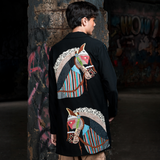 Person wearing a black jacket with colorful horse designs in an urban setting.