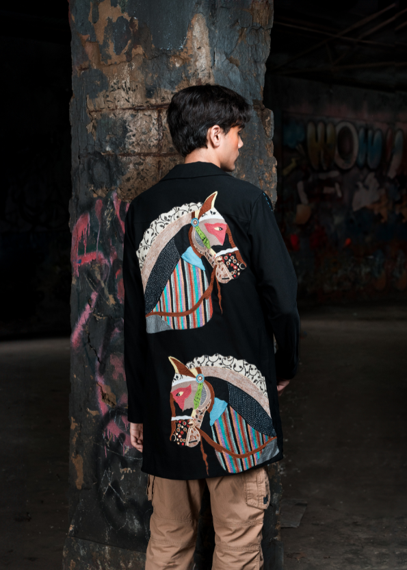 Person wearing a black jacket with colorful horse designs in an urban setting.