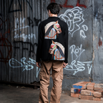 Person wearing a black sweatshirt with a colorful horse design, standing in front of a graffiti-covered wall.