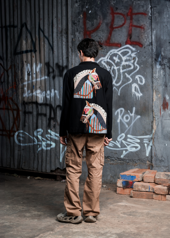 Person wearing a black sweatshirt with a colorful horse design, standing in front of a graffiti-covered wall.