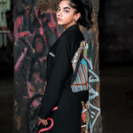 Woman wearing a black kimono with colorful designs against a graffiti-covered wall.