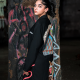 Woman wearing a black kimono with colorful designs against a graffiti-covered wall.