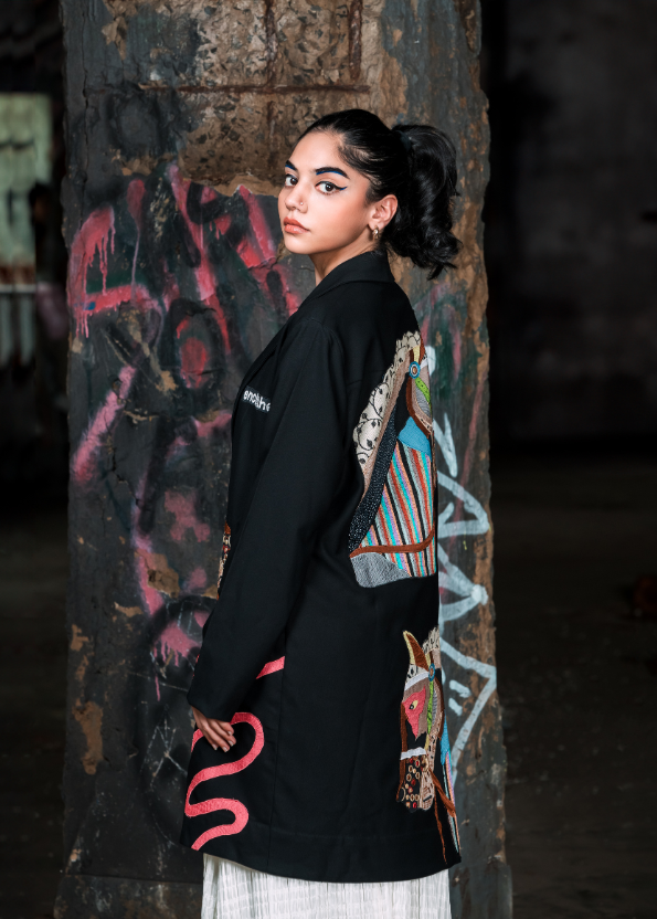 Woman wearing a black kimono with colorful designs against a graffiti-covered wall.