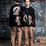 Two individuals wearing matching outfits with colorful designs in front of a graffiti-covered wall.