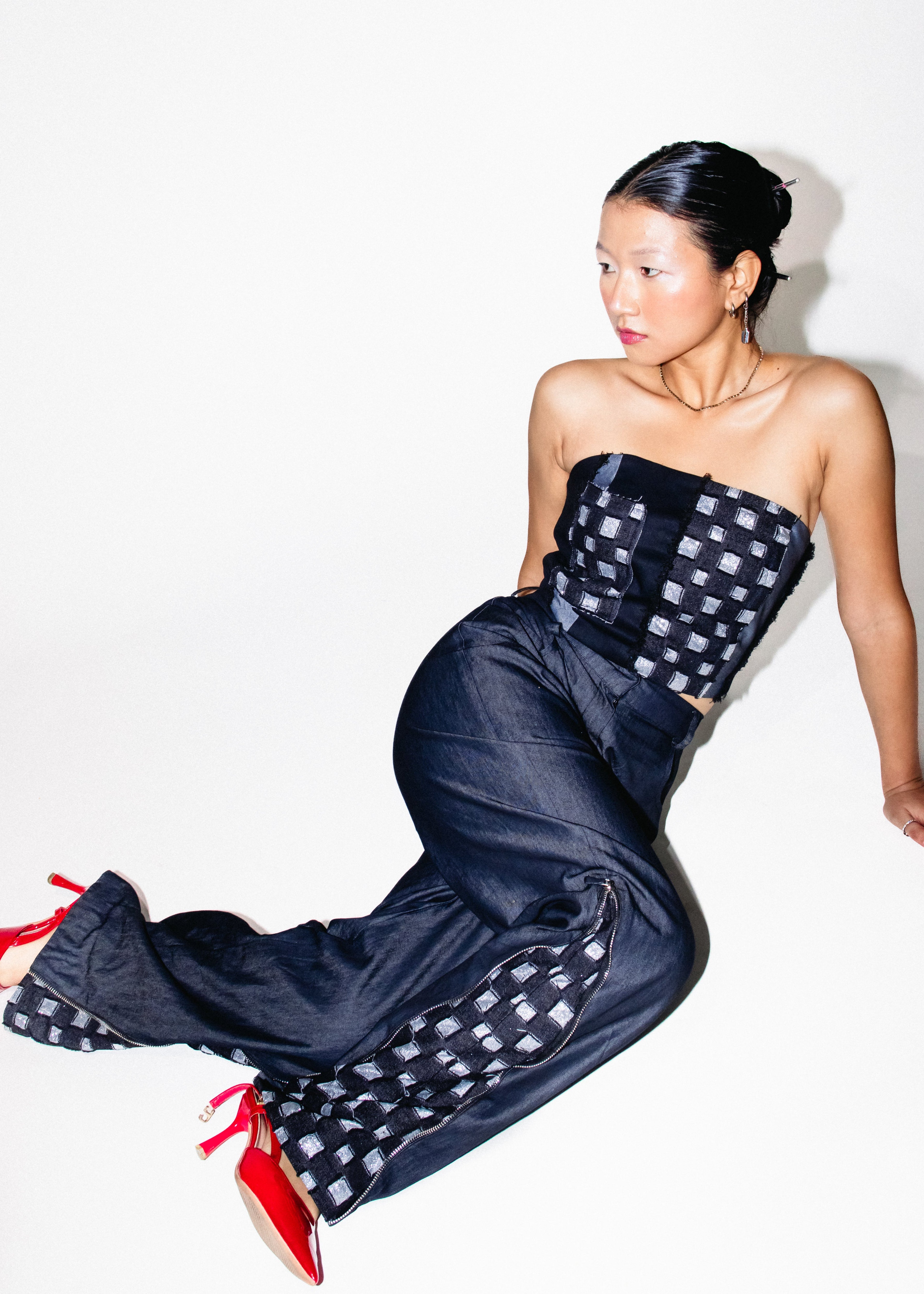 Woman wearing a strapless black and white checkered dress with red shoes on a white background