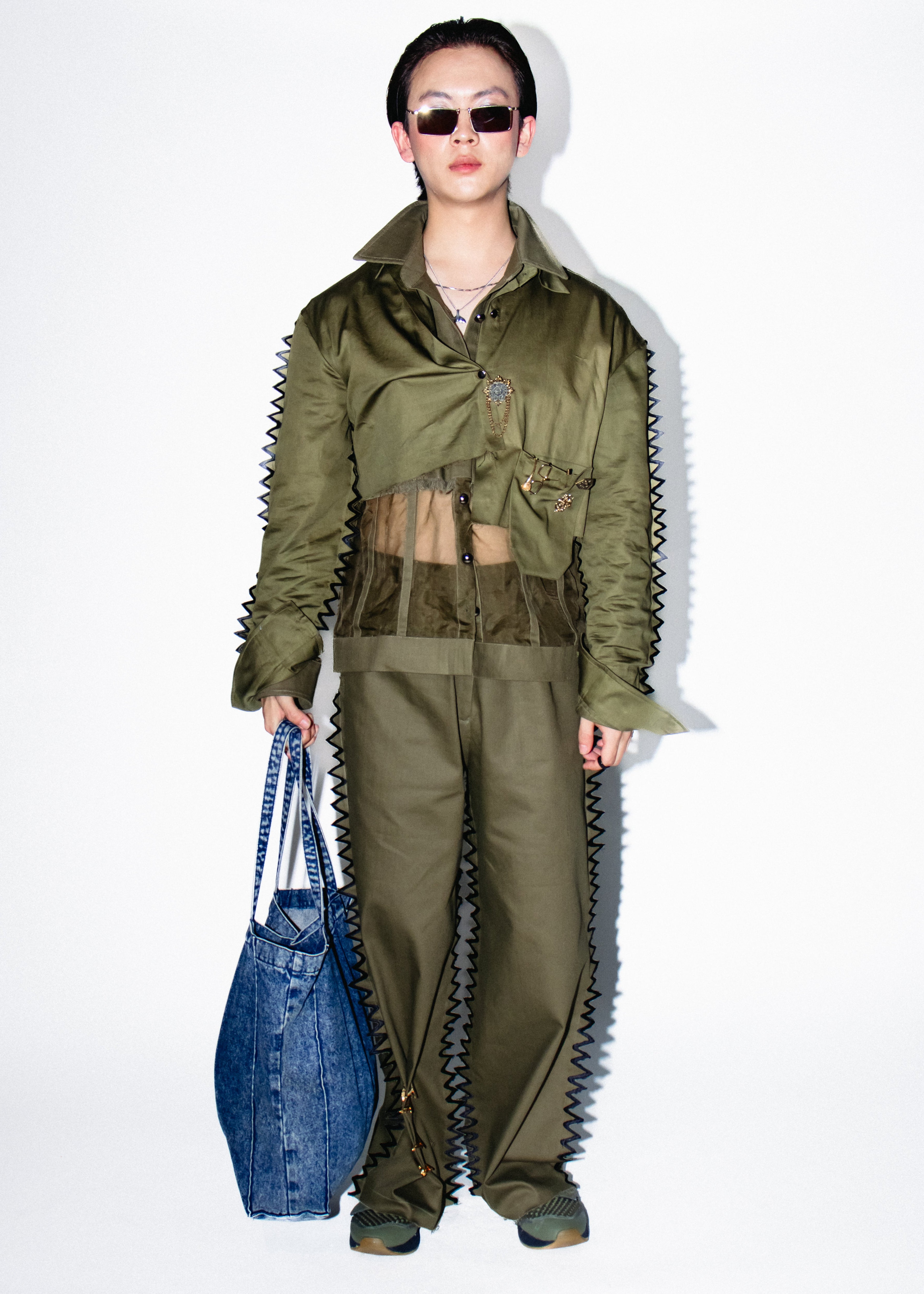 Person wearing a green military-style outfit with a blue bag on a white background