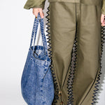 Person wearing a green outfit with zigzag details holding a blue denim bag on a white background