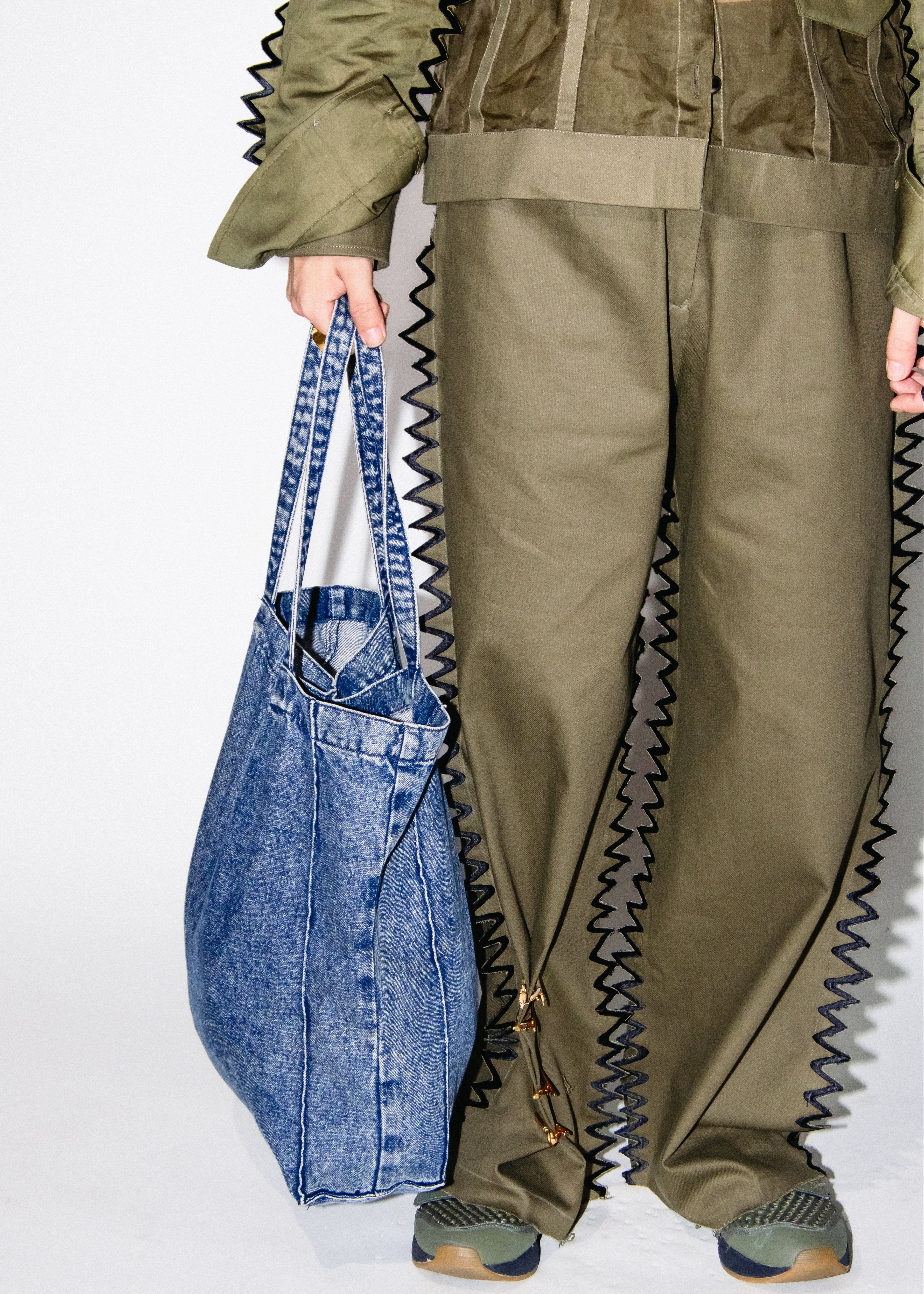 Person wearing a green outfit with zigzag details holding a blue denim bag on a white background