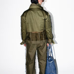 Person wearing a green military-style outfit with spiky details, holding a blue bag on a white background.