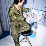 Person in military-style outfit sitting at a sewing machine.