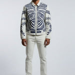 Person wearing a patterned jacket and white pants on a gray background
