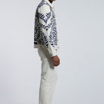 Man wearing a patterned jacket and white pants on a gray background