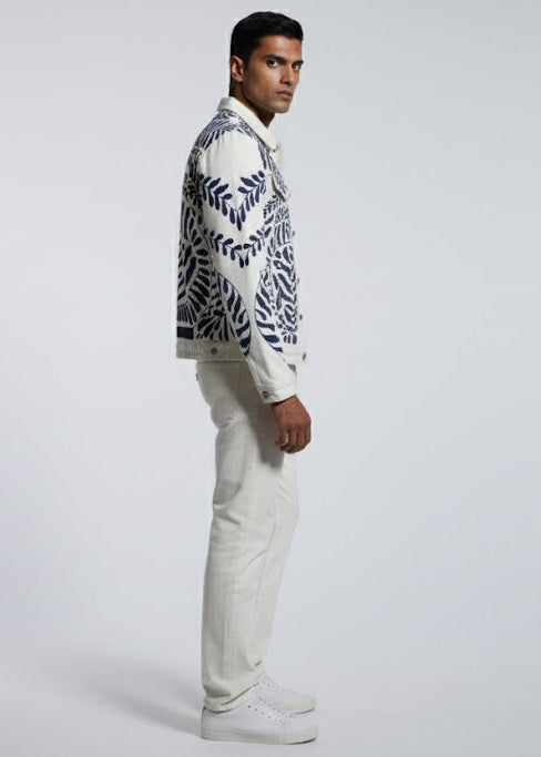 Man wearing a patterned jacket and white pants on a gray background