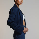 Woman wearing a navy blue jacket and denim skirt on a plain background
