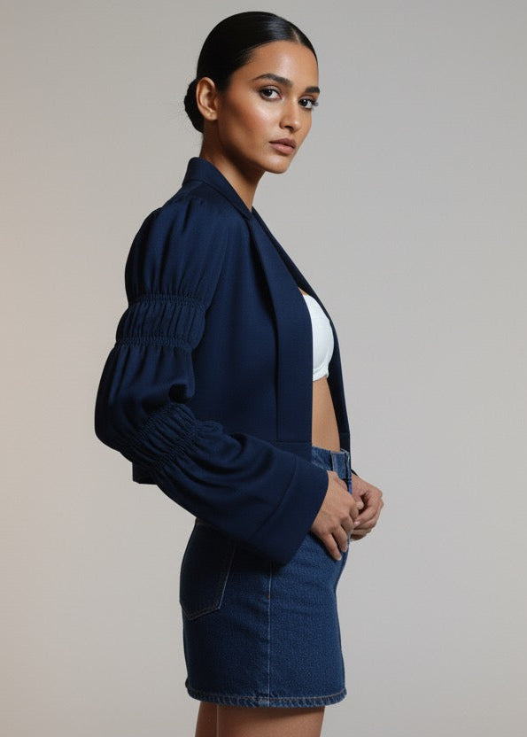 Woman wearing a navy blue jacket and denim skirt on a plain background