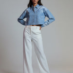 Woman wearing a denim jacket and white pants against a plain background