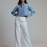 Woman wearing a denim jacket and white pants against a plain background
