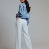 Woman wearing a blue jacket and white pants against a plain background