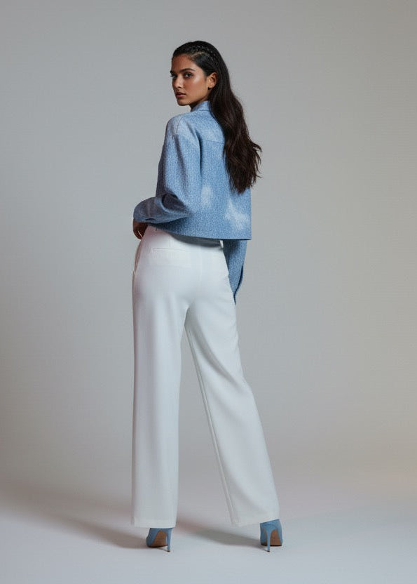 Woman wearing a blue jacket and white pants against a plain background