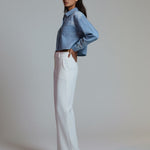 Woman wearing a blue denim jacket and white pants on a plain background