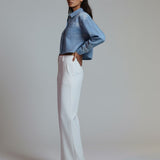 Woman wearing a blue denim jacket and white pants on a plain background