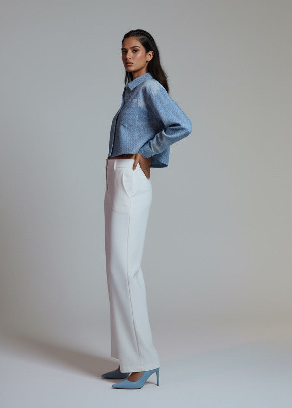 Woman wearing a blue denim jacket and white pants on a plain background