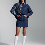 Woman wearing a blue floral blouse and denim skirt with white knee-high socks against a gray background